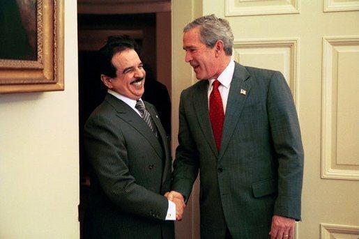 Un an et demi après la photo précédente, le roi du Bahreïn est de nouveau en visite officielle aux États-Unis. Il est ici reçu par le président George W. Bush, hilare, dans le Bureau Ovale le 29 novembre 2004. Il est notable que le roi ne s'habille pas en tenue de cheikh mais en costume occidental lorsqu'il va visiter ses supérieurs hiérarchiques. Soumission symbolique de type vestimentaire à laquelle n'a pas eu droit le pauvre François Hollande.